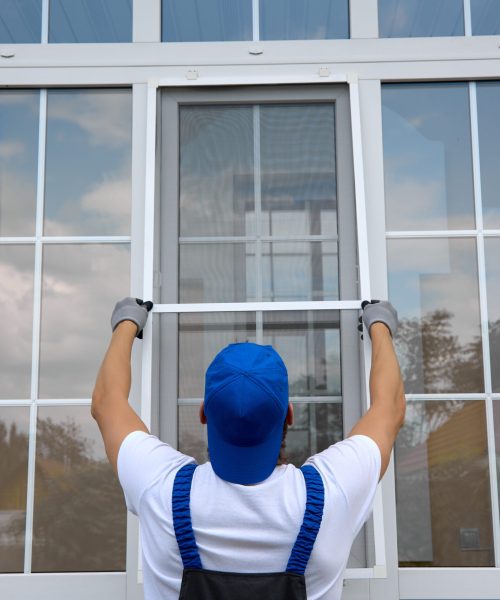 Professional installation of an additional insect net on the window Background of blue-cap worker installing a mosquito net on large plastic window outside the building in summer. Professional installation of an additional insect net on window